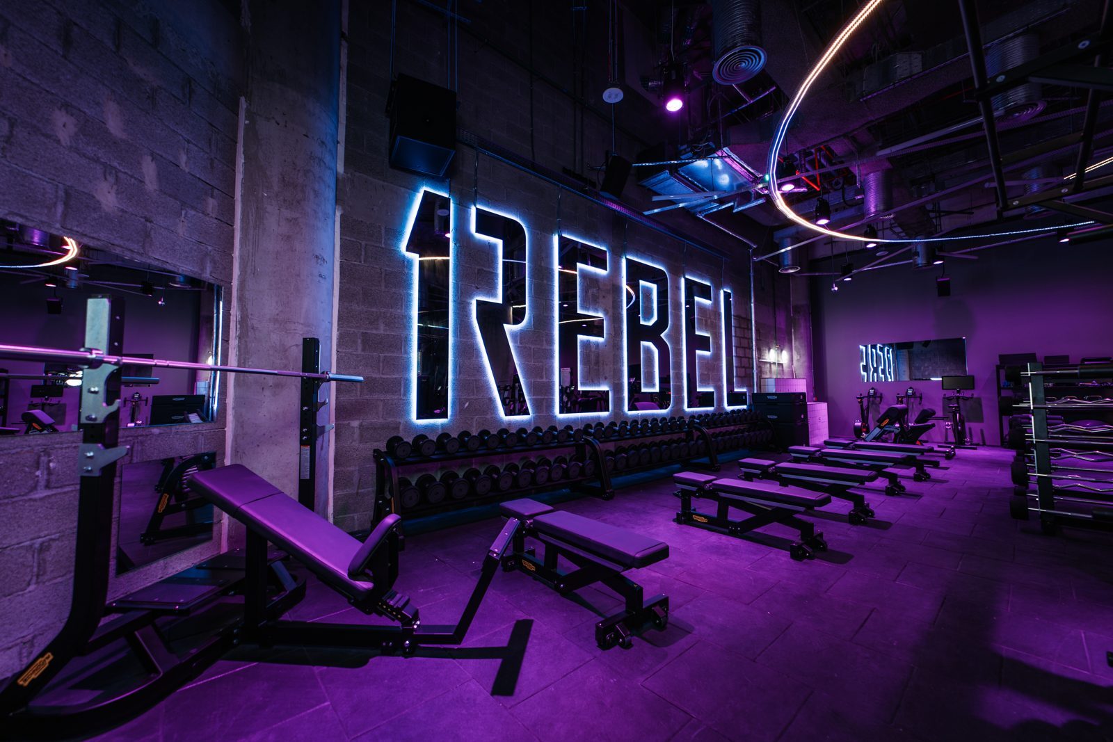The 1Rebel studio at ICD Brookfield Place, with its lit 1REBEL sign above benches and dumbbell racks under purple light
