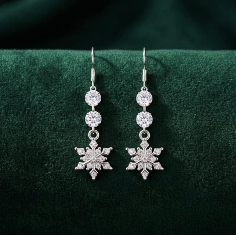 A pair of silver drop earrings set with crystals and a snowflake charm, on green velvet