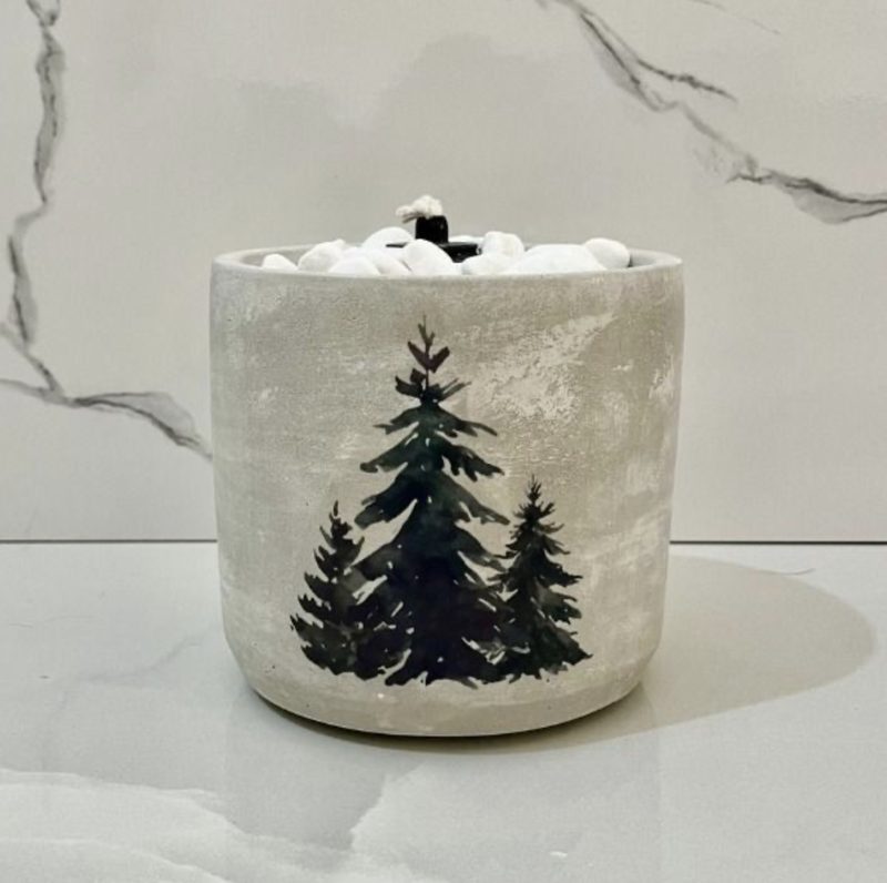 A grey concrete pot printed with three pine trees and filled with white pebbles