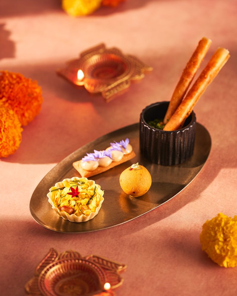 A chiwda tart and a chakli cigar on a brass tray with diyas and marigolds