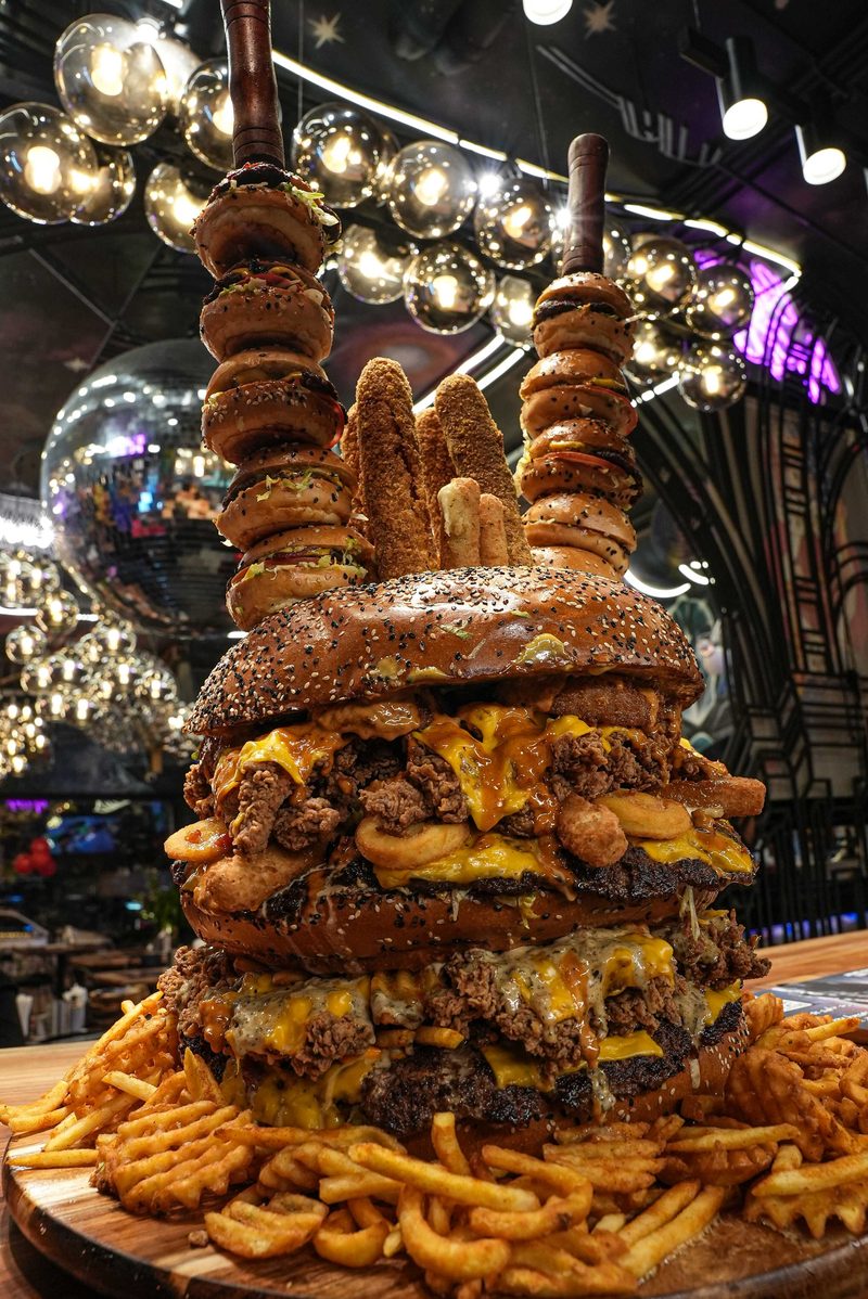 A towering burger stack skewered with sticks and served with a pile of fries