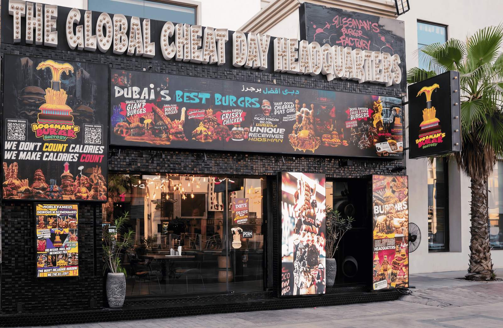 The storefront of Bossman's Burgr Factory on Jumeirah Beach Road, covered in colourful burger signage, with a palm tree beside it