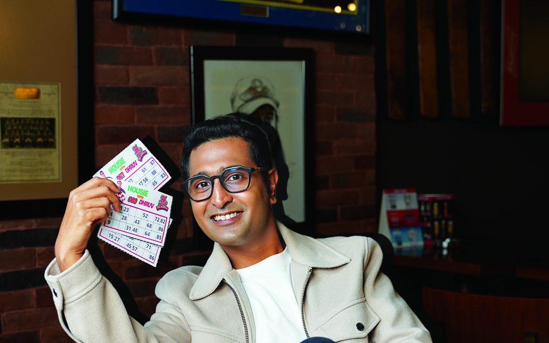 Dhruv, the host of Housie Night, smiling in a pub and holding up a handful of housie tickets
