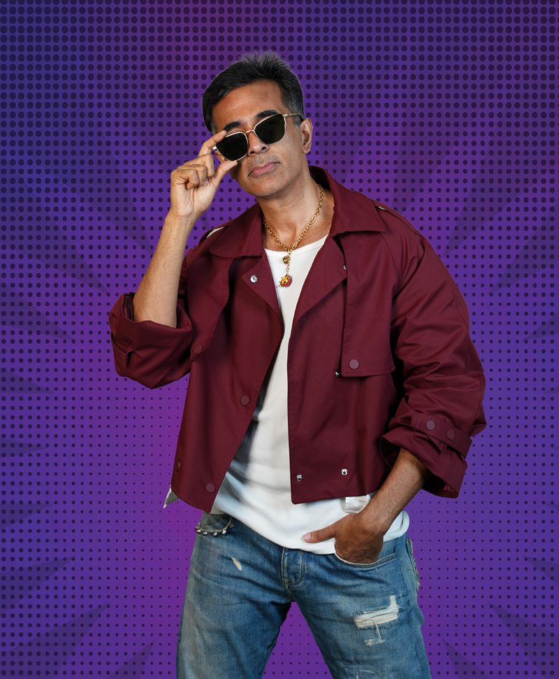 Loki, the host of the Bollywood quiz, in sunglasses and a maroon jacket against a purple dotted backdrop