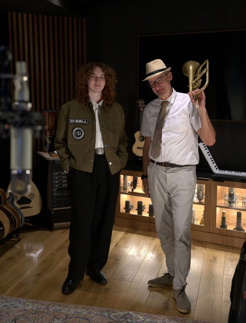 D-BELL in a recording studio beside a musician holding a trumpet