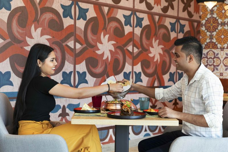 A couple sharing Indian dishes at a table in front of a patterned wall