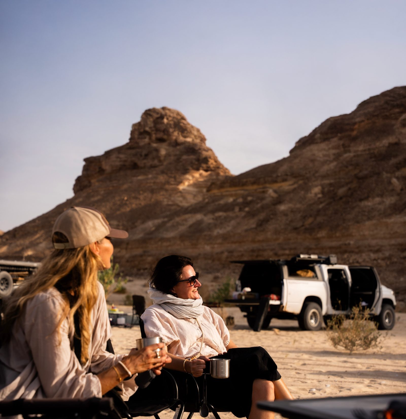Two travellers relax in camp chairs beside a 4x4 at a desert camp on a Dunes and Stars expedition