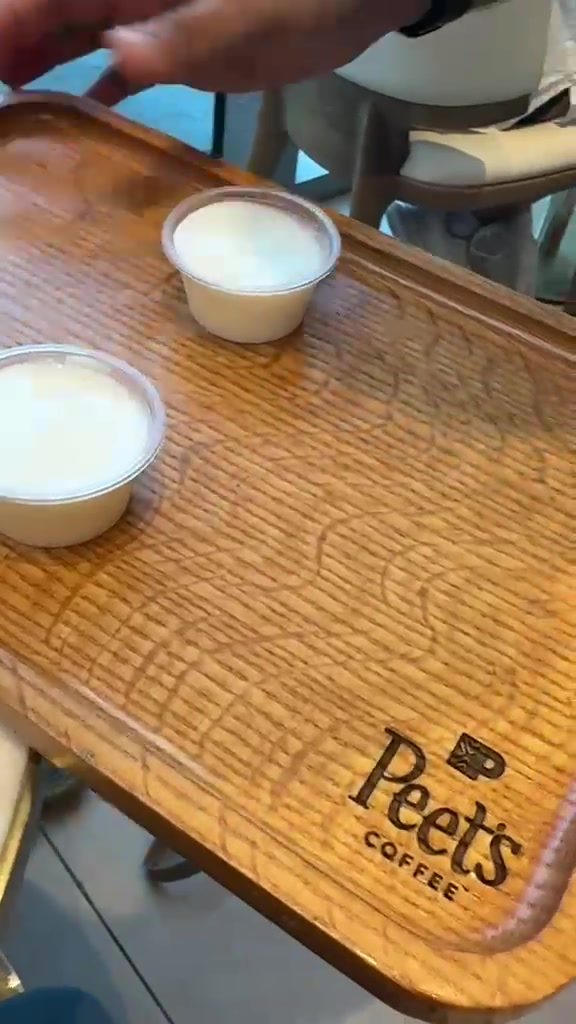 Two small cups of milk on a wooden Peet's Coffee tray at Dubai Harbour