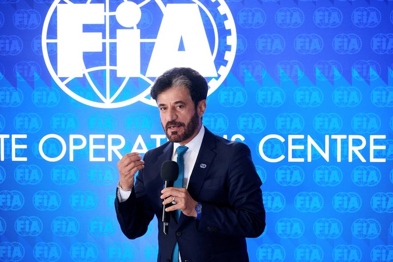 FIA President Mohammed Ben Sulayem speaking into a microphone in front of an FIA backdrop