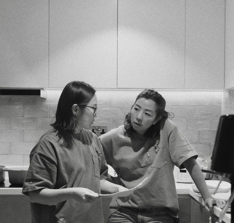 Black and white photograph of Five Spice founders Xini and Starry talking in a kitchen