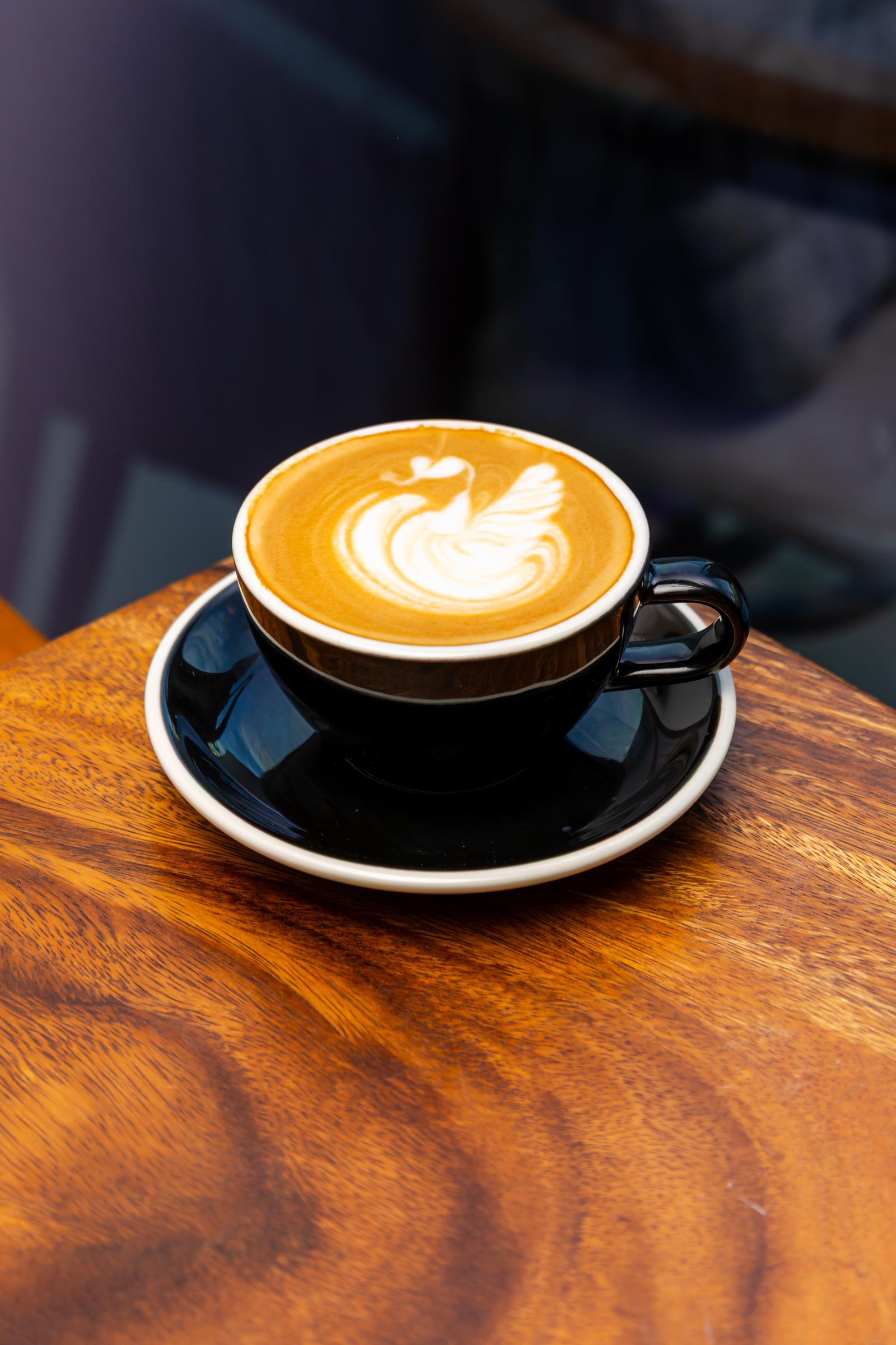 A cup of cappuccino with latte art on a black saucer, on a wooden table