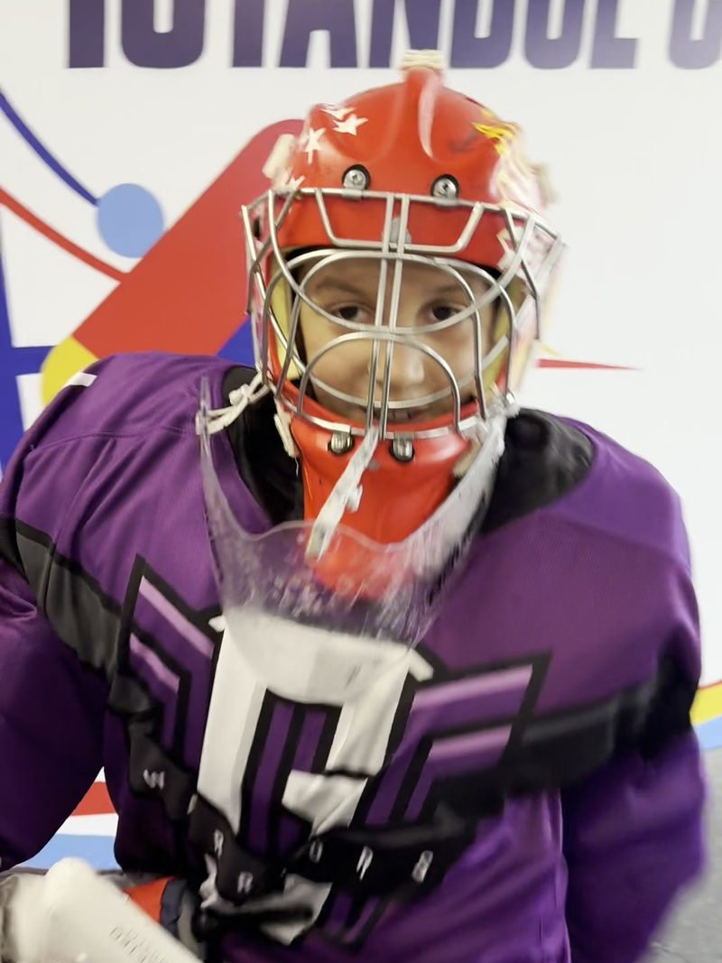 A Galaxy Warriors goalie in a red mask and purple jersey in front of the Istanbul Cup wall
