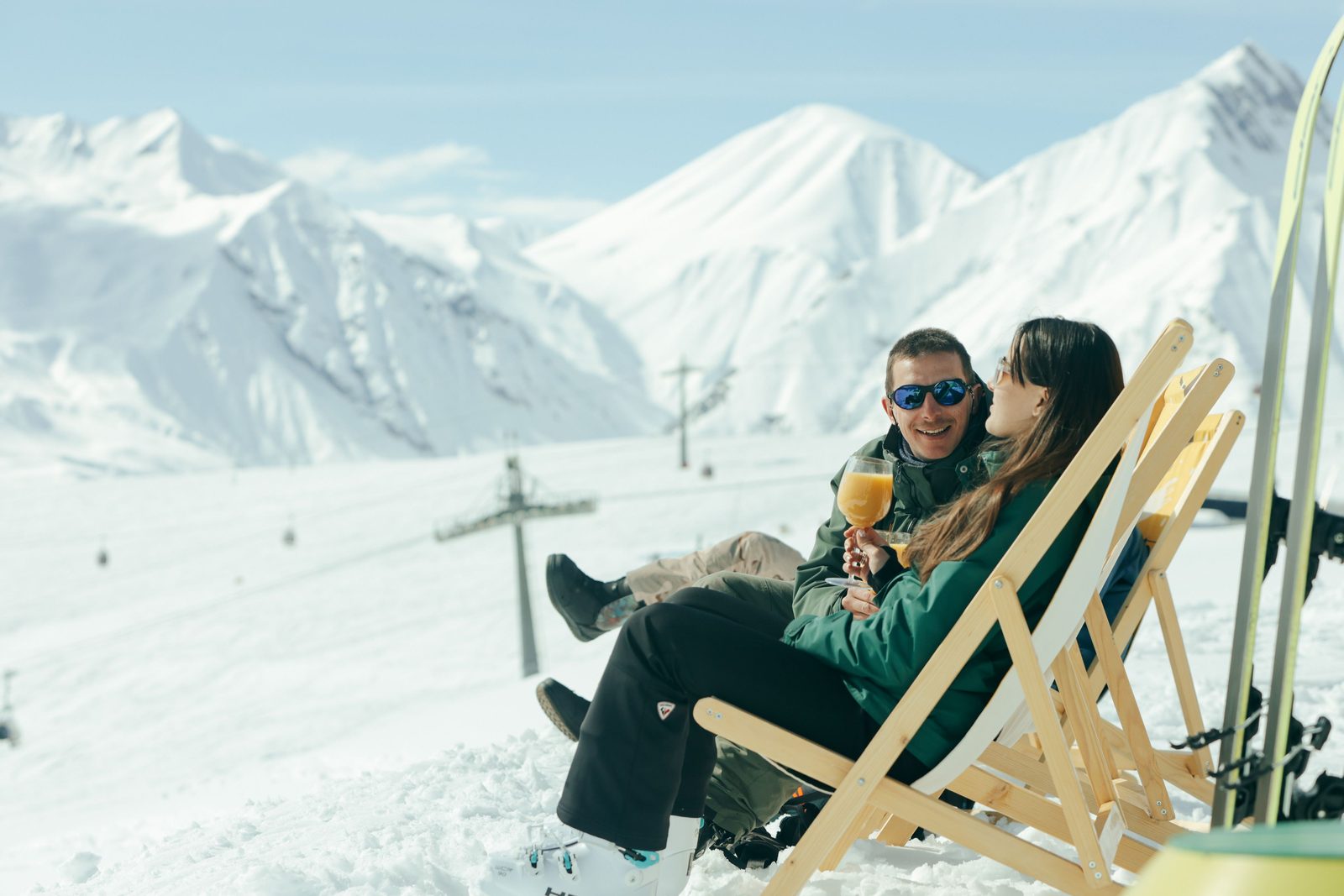 A couple relaxing in deckchairs with a drink on a snowy mountain slope