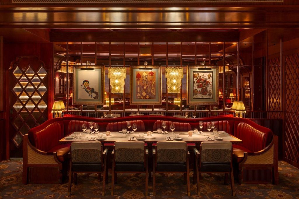 A long dining table laid with glasses and plates in front of red leather banquette seating, with three framed