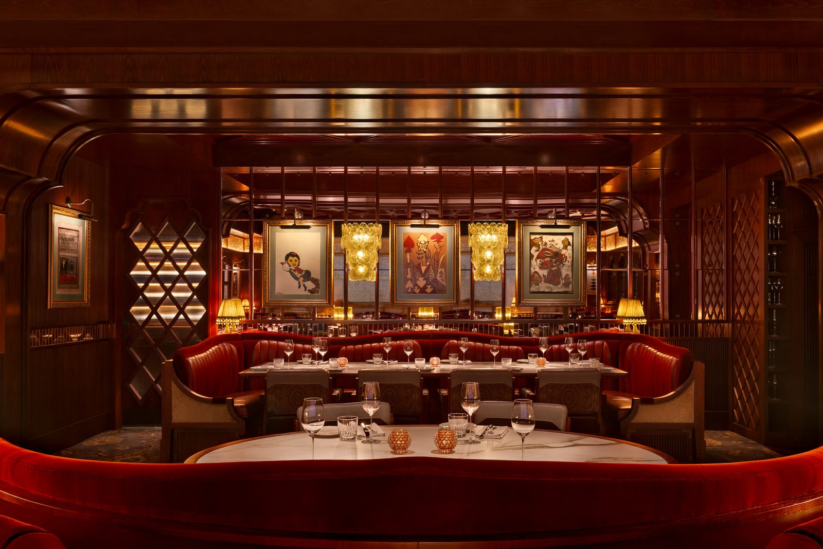 Dining room at Gymkhana Dubai with dark wood panelling, red leather banquettes, framed artwork and warm amber table lamps