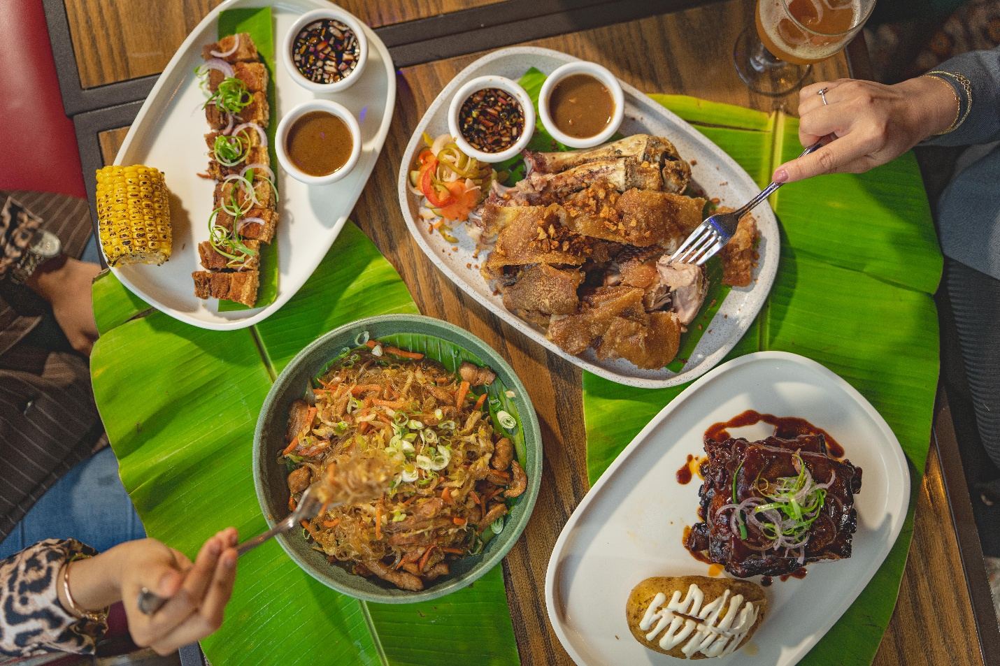A banana-leaf table spread with Filipino dishes, grilled corn and dipping sauces as guests reach in with their hands