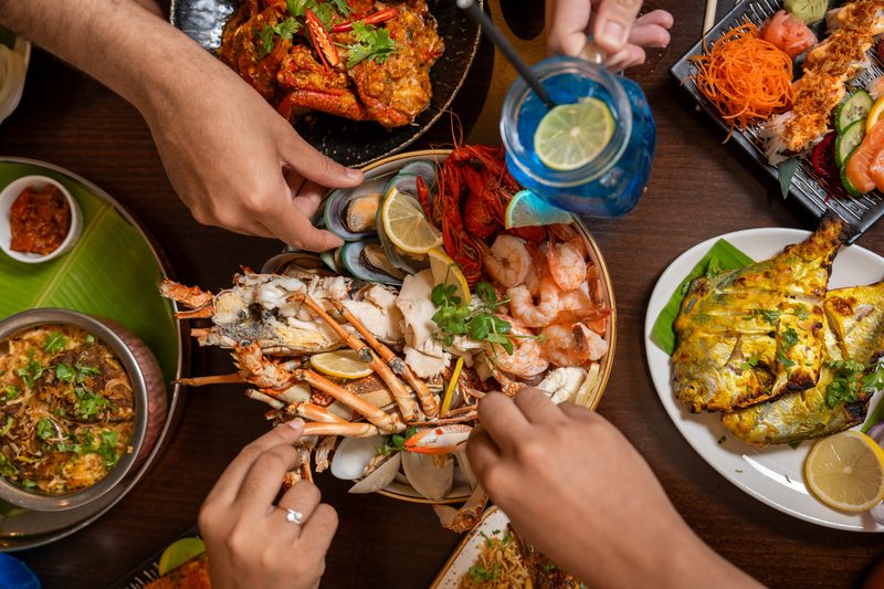 Hands reaching across a table for a platter of seafood and shared dishes at Khayal
