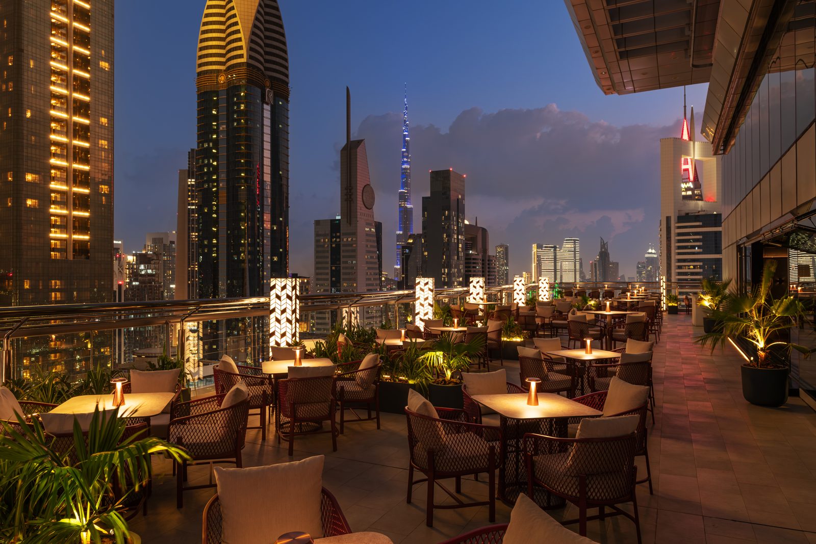 The terrace of Level 43 Sky Lounge at dusk, with tables and lanterns in front of the lit Dubai skyline