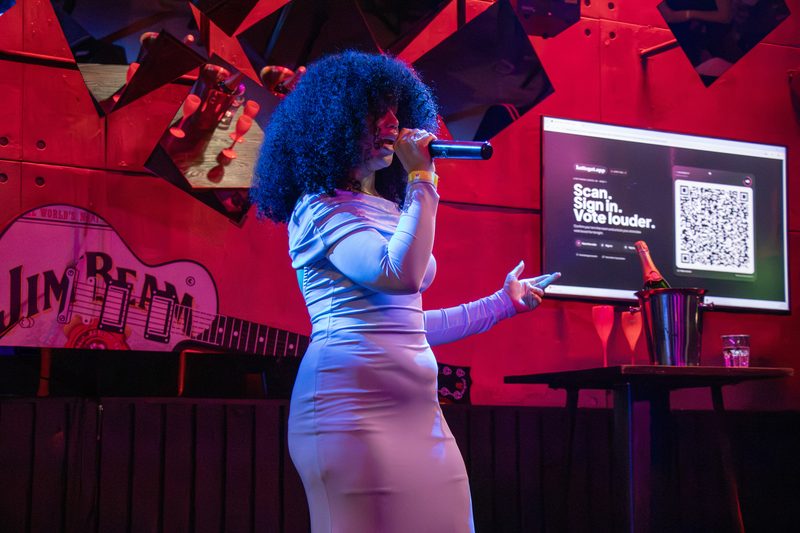 A singer with a microphone performing on the Lucky Voice stage beside a screen showing a QR code