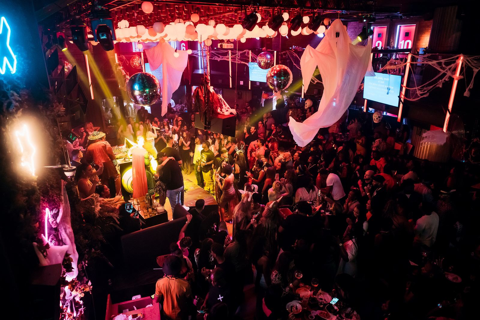 A crowded Lucky Voice venue seen from above, with white ghost decorations, cobweb-style hangings, neon lighting and a large crowd gathered around the stage