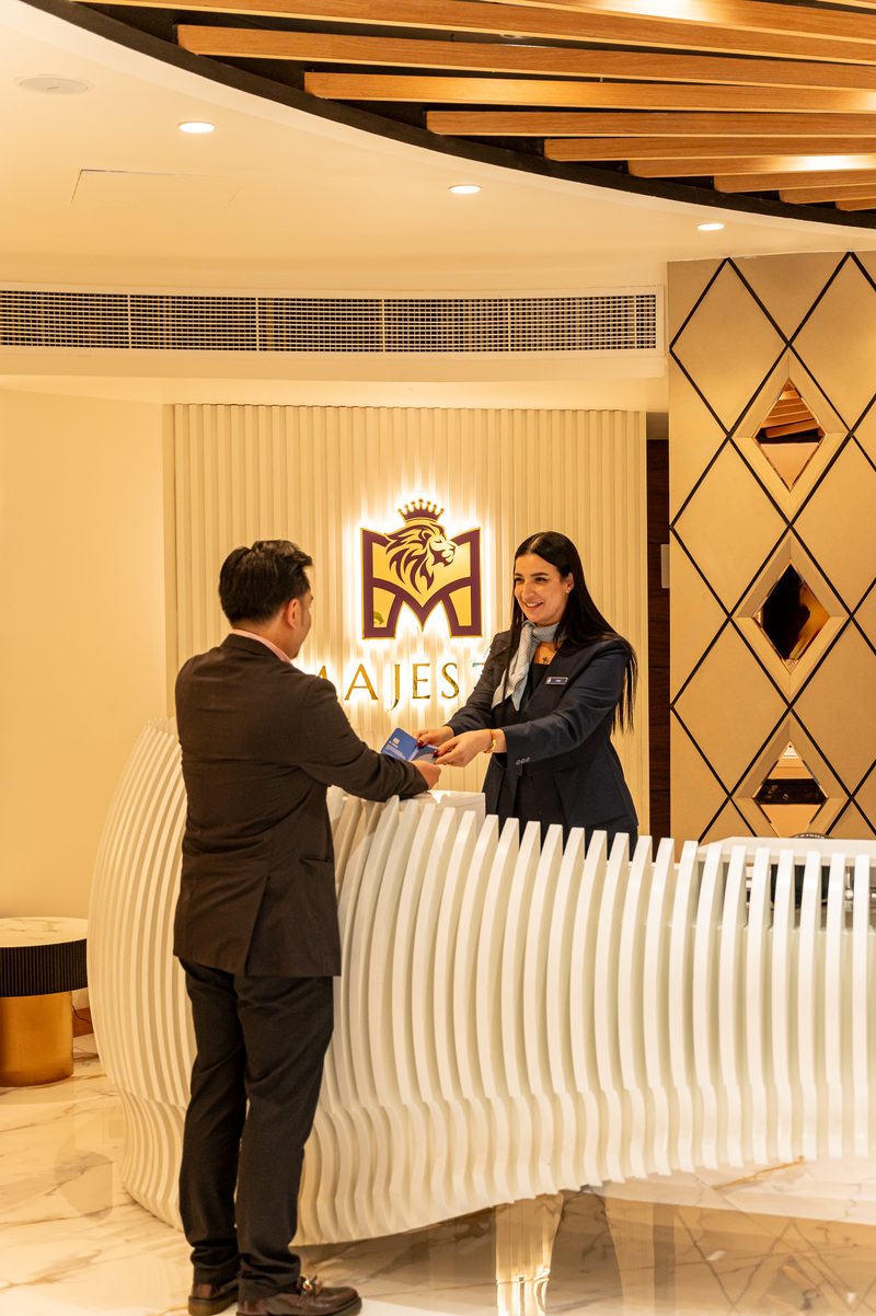 A guest being welcomed at a curved white reception desk under the Majestic crest