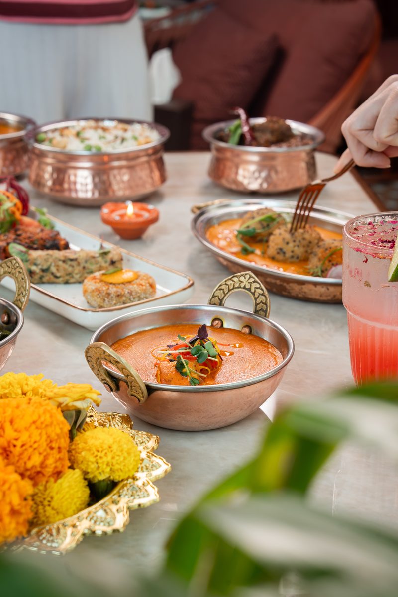 A copper bowl of curry, marigolds and a pink drink on a table set for Diwali at Mausam