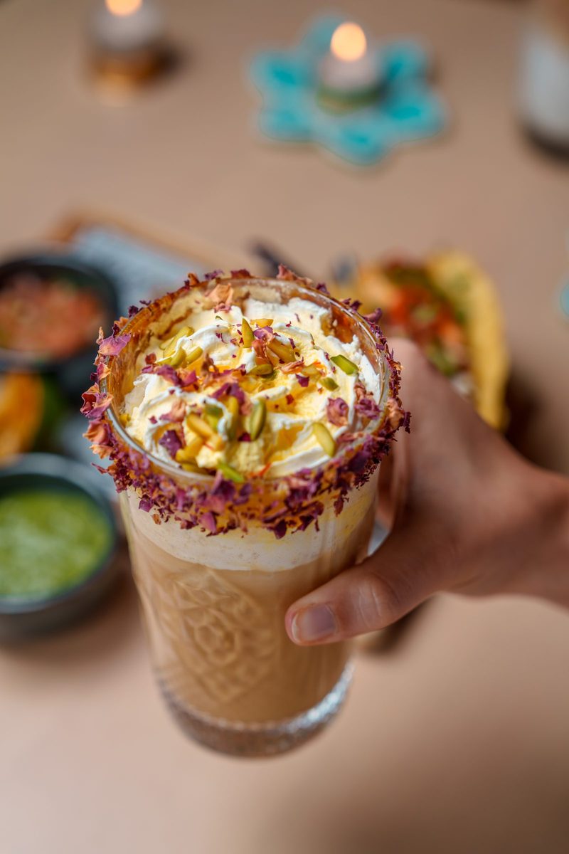 An iced drink topped with cream, pistachio and rose petals, photographed for the hotel’s Diwali menu