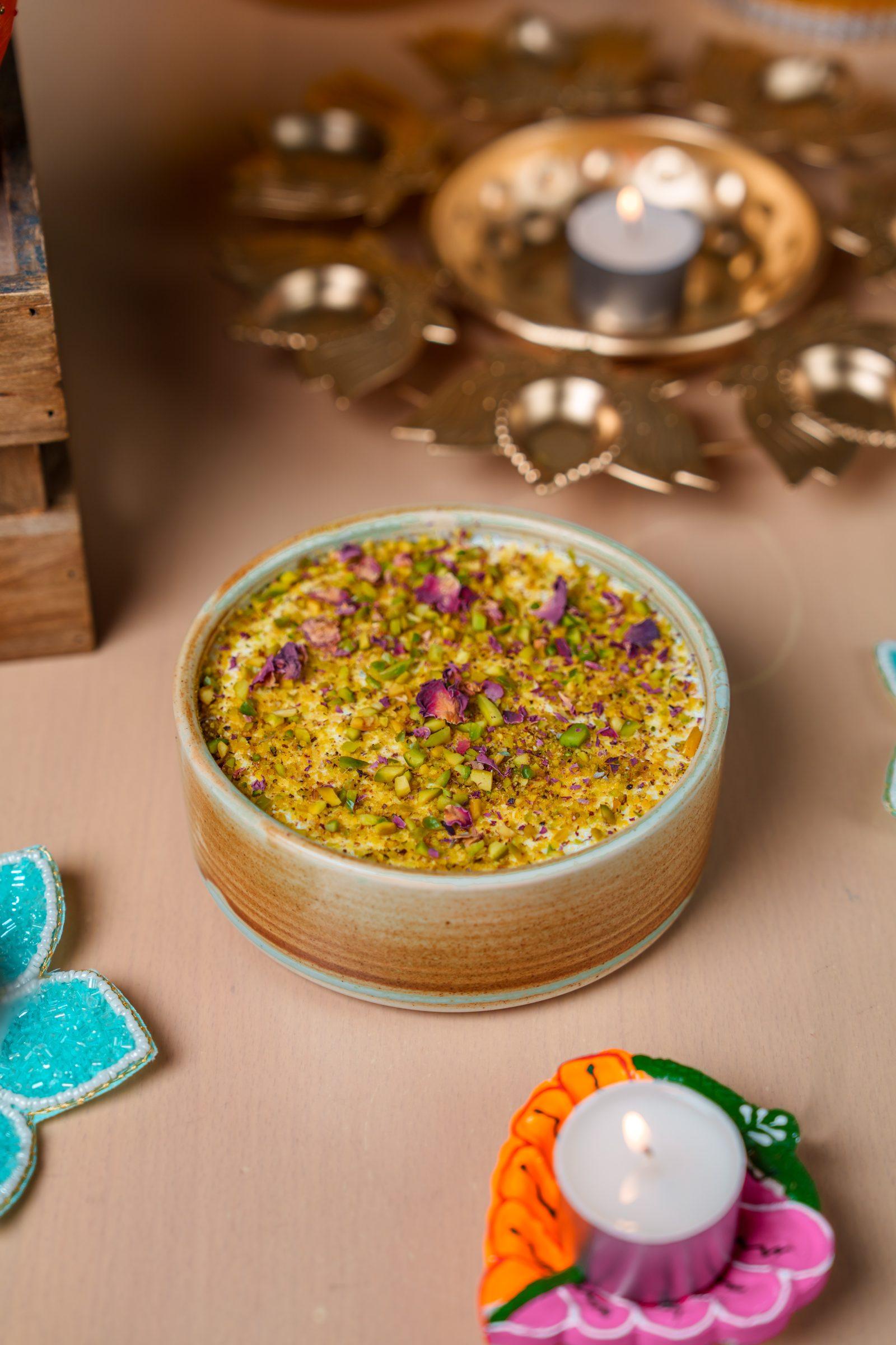 A pistachio and rose petal dessert beside lit diyas, photographed for the Diwali menu at Mövenpick Hotel Apartments Downtown Dubai