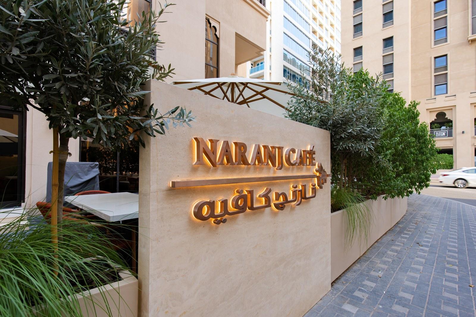 The Naranj Cafe sign and outdoor terrace with white parasols at DoubleTree by Hilton Dubai Al Jadaf