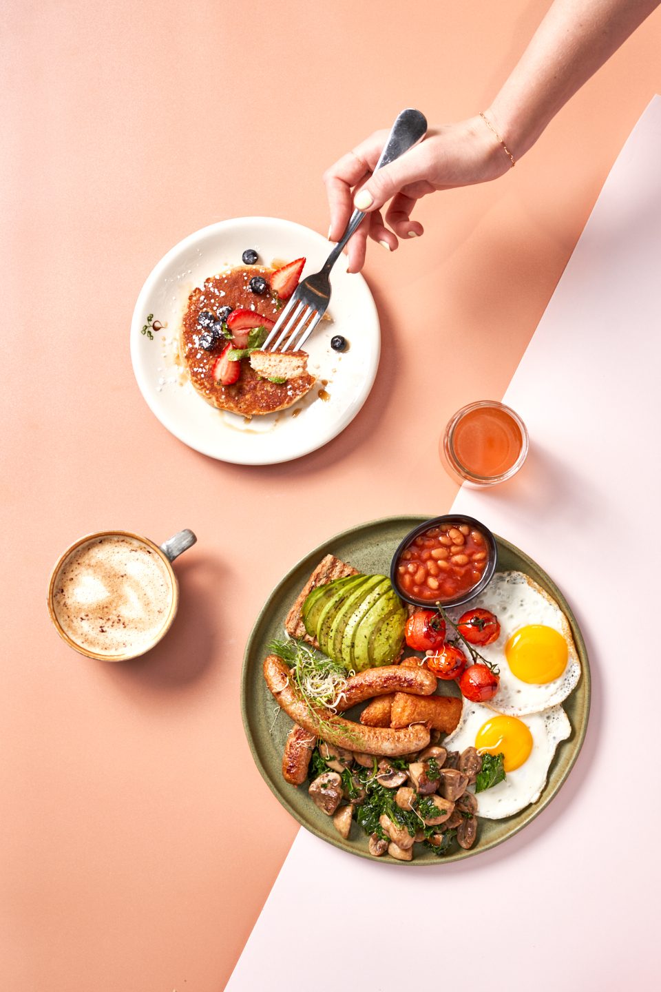 A Classic English Breakfast with eggs, sausages, beans and avocado toast beside a pancake and a coffee at Organic Foods & Café