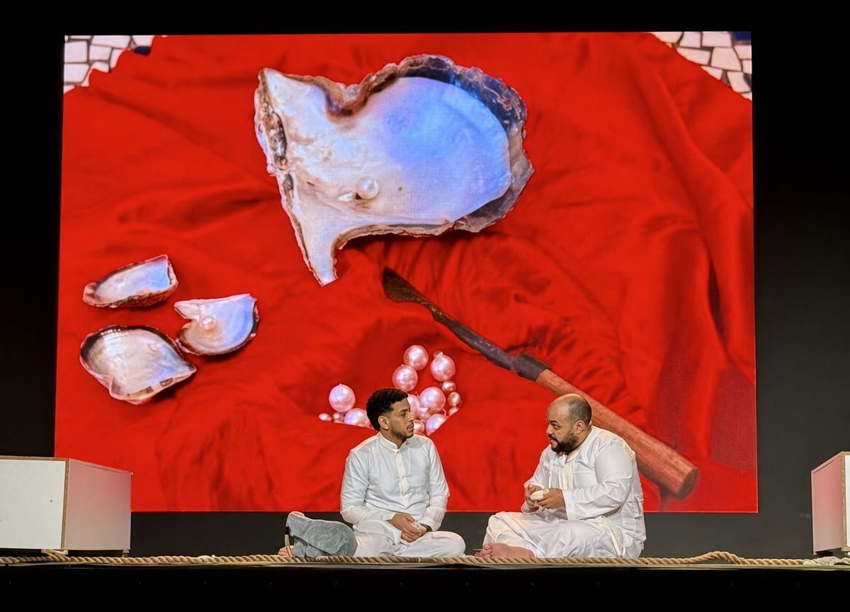 Two actors in white seated on stage in front of a pearl shell backdrop in The Pearl Diver