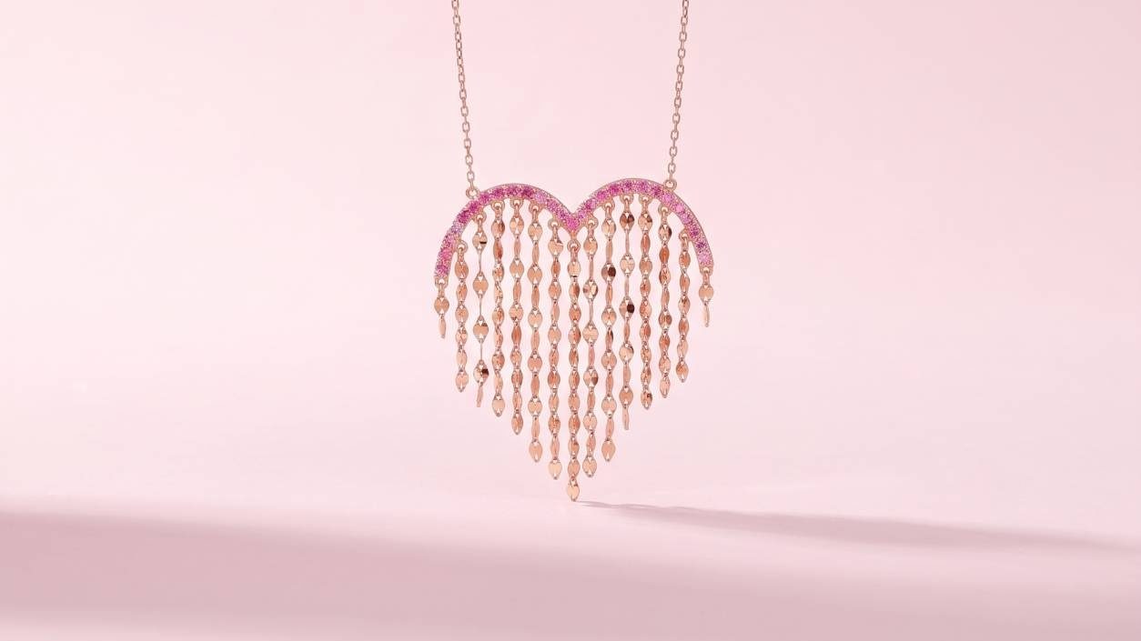 A rose gold heart-shaped necklace with pink sapphire strands hanging against a soft pink background