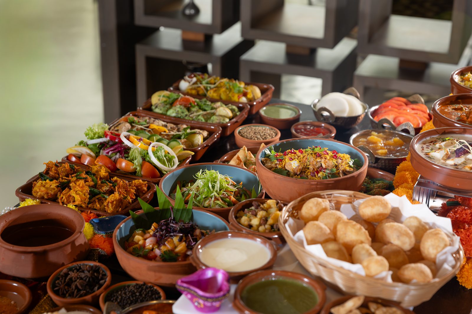 A Diwali buffet table with Indian dishes in clay and copper bowls, puri, chutneys and marigold flowers