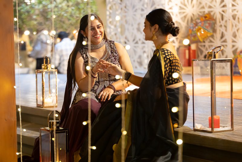 Two guests in festive dress seated at a table lit by string lights