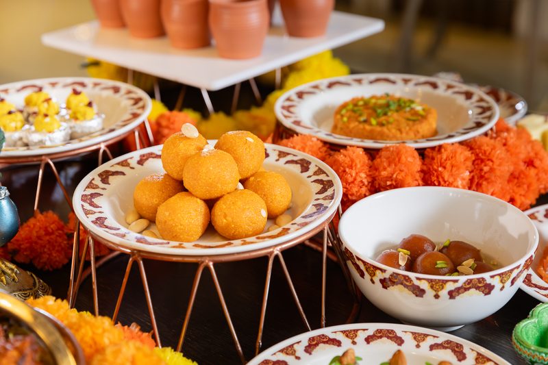 Plates of laddoo and other Indian sweets on stands among marigold flowers at the Diwali brunch