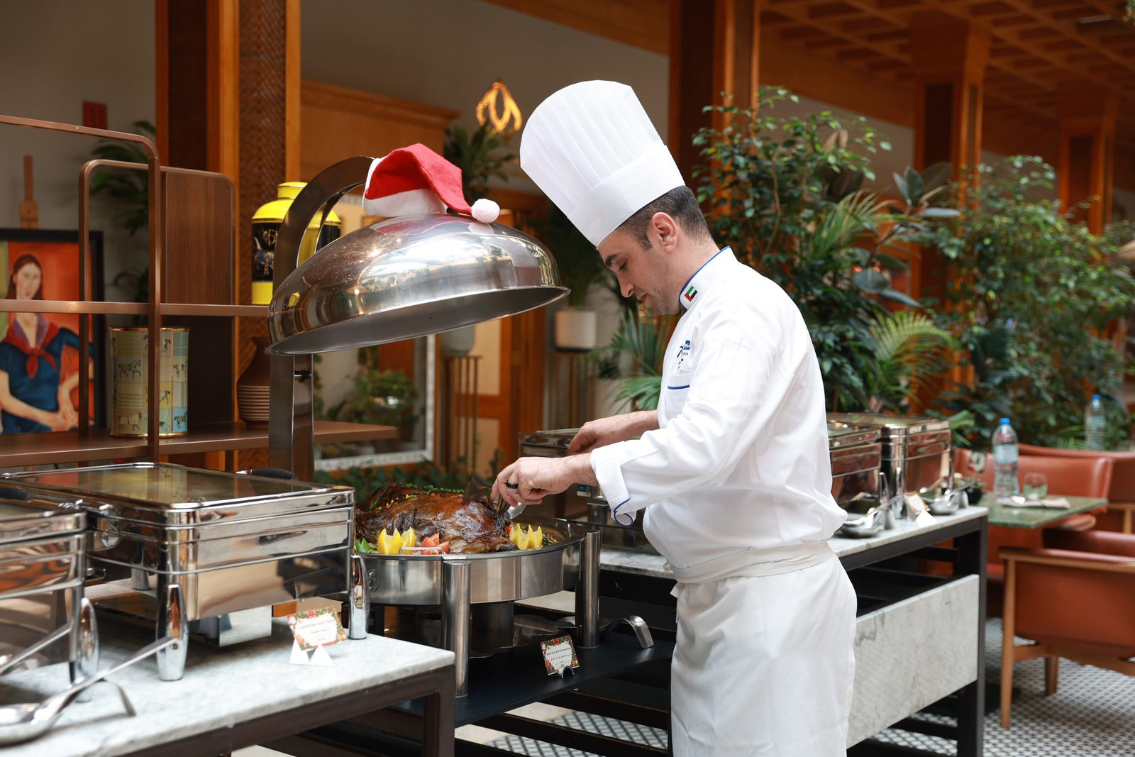 A chef in a white hat lifting a cloche over a hot buffet station