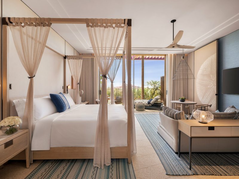 A bedroom with a canopy bed and white drapes, a sofa and a sliding view out to a terrace