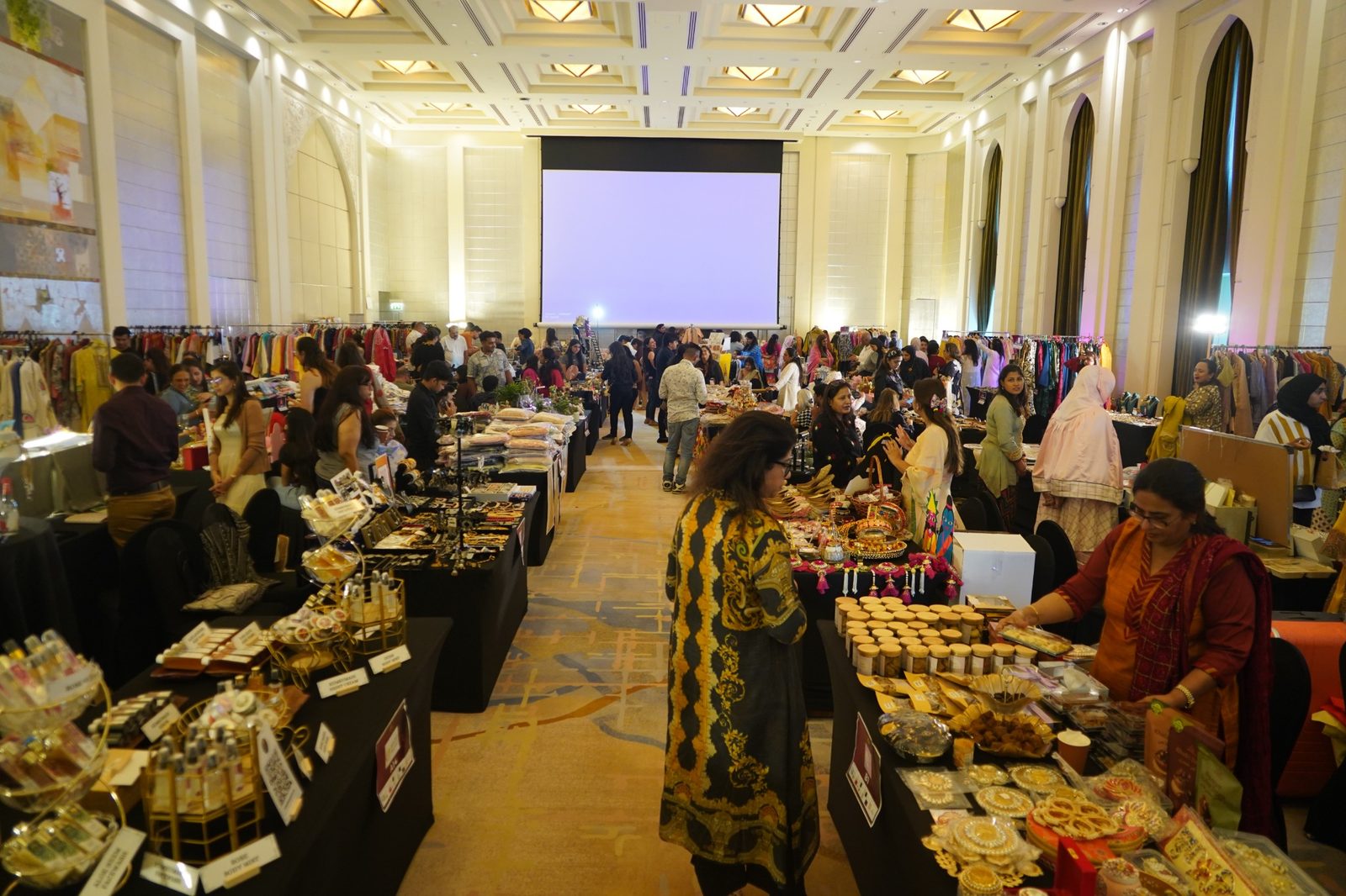 A wide view of a ballroom filled with exhibition stalls and visitors browsing, at a previous Miracle exhibition