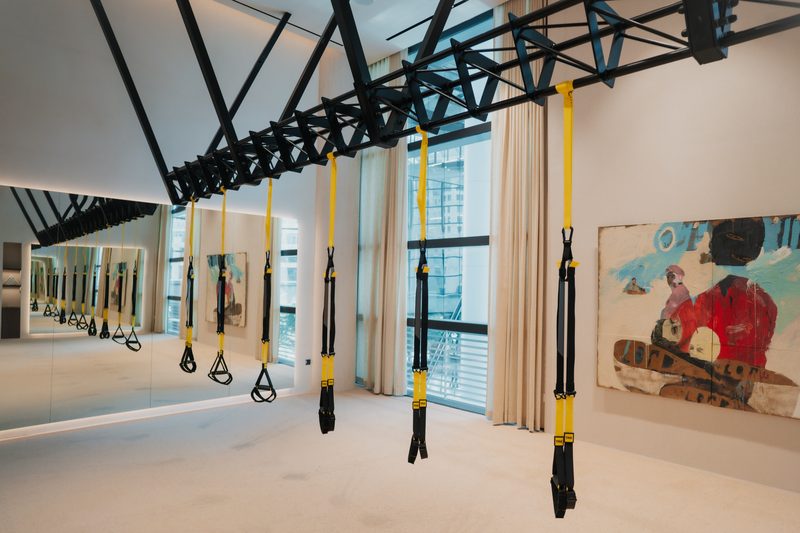 The multi-room studio at Reform Athletica with suspension straps hanging from a steel frame and a large painting on the wall