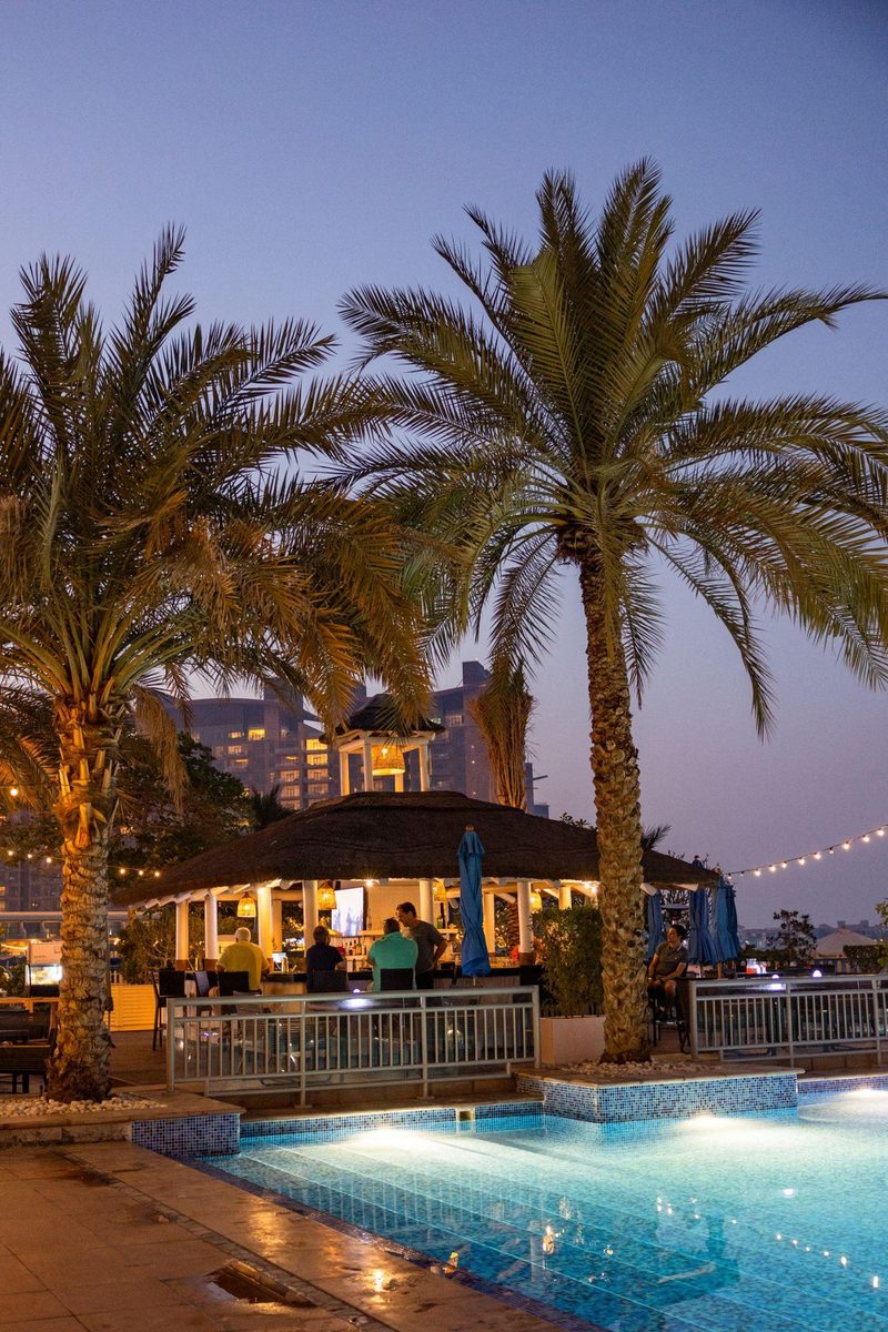 Palm trees and the beach bar pavilion beside the pool at Riva Beach Club at dusk