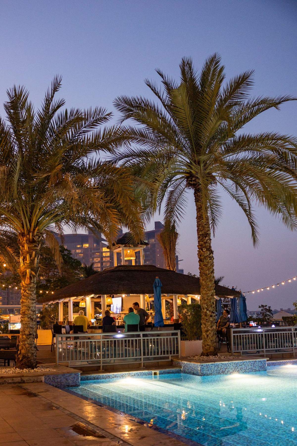 Palm trees and the beach bar pavilion beside the pool at Riva Beach Club at dusk