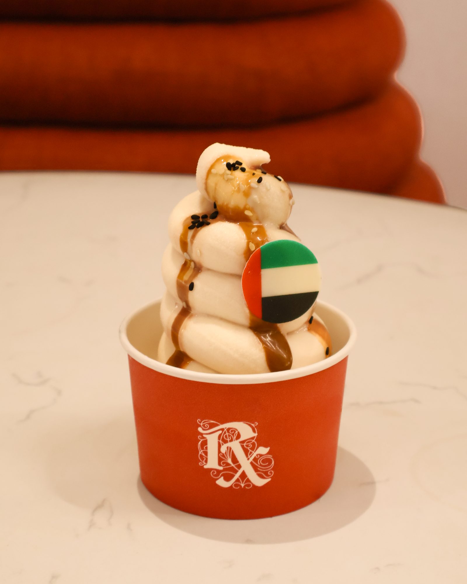 A swirl of Qahwa Soft Serve with a UAE flag disc in a red RX Coffee Apothecary cup