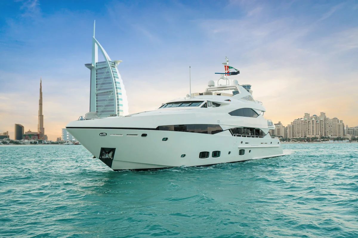 A large white motor yacht on turquoise water with the Burj Al Arab and the Dubai coastline behind it