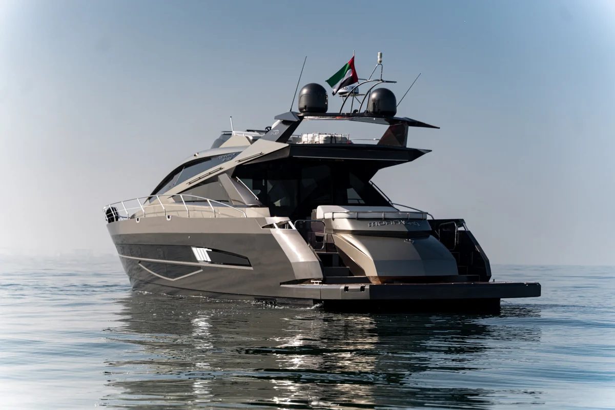 A grey and black motor yacht with two radar domes and a UAE flag, on calm water