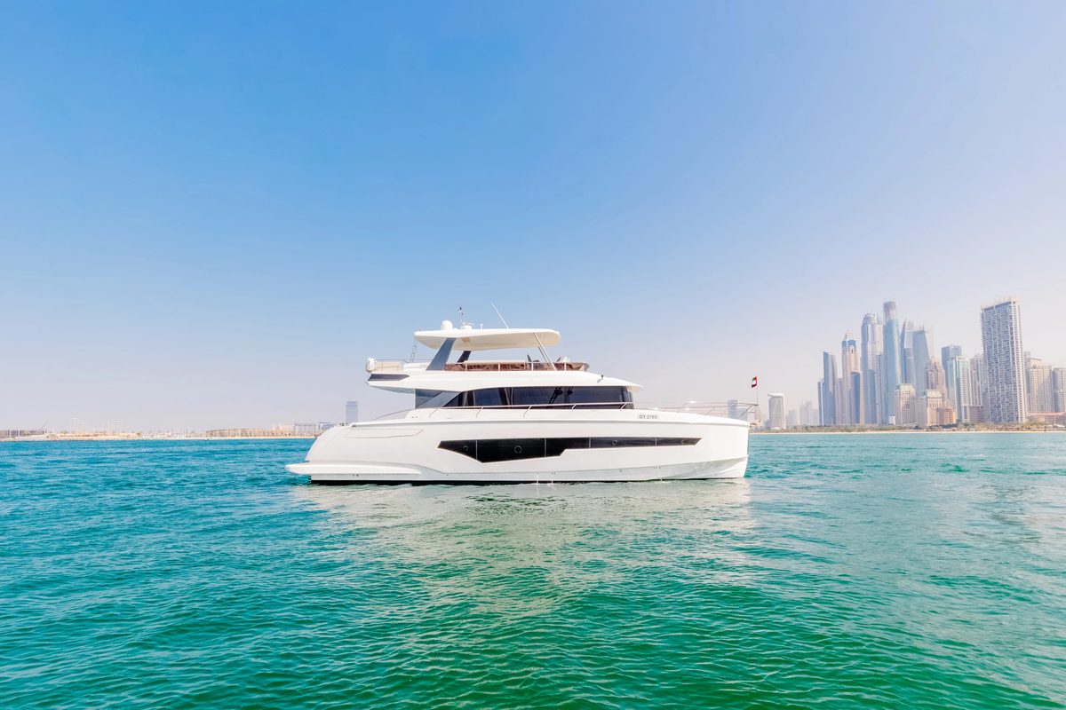A white and grey motor yacht on calm turquoise water with the Dubai Marina skyline in the distance