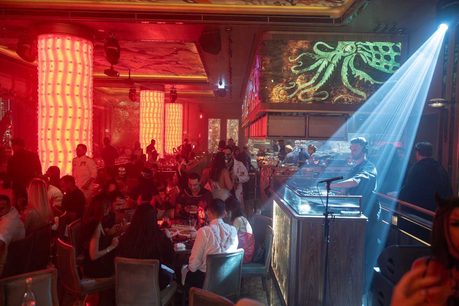 Guests dining under red-lit columns as a DJ plays beside a beam of blue light at Sexy Fish Dubai