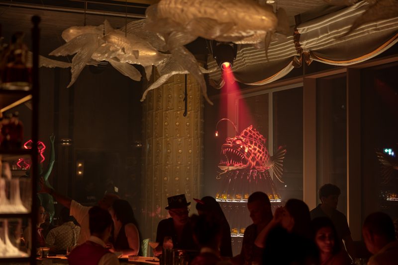 The Sexy Fish Dubai dining room, with a glowing anglerfish light and sculptural fish overhead and guests seated below