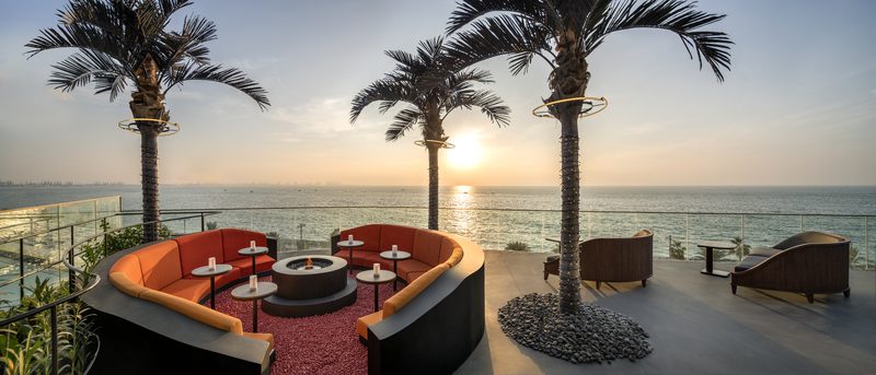 Curved orange sofas around a fire pit on the SoBe terrace at W Dubai - The Palm, with two palm trees and the sea at sunset