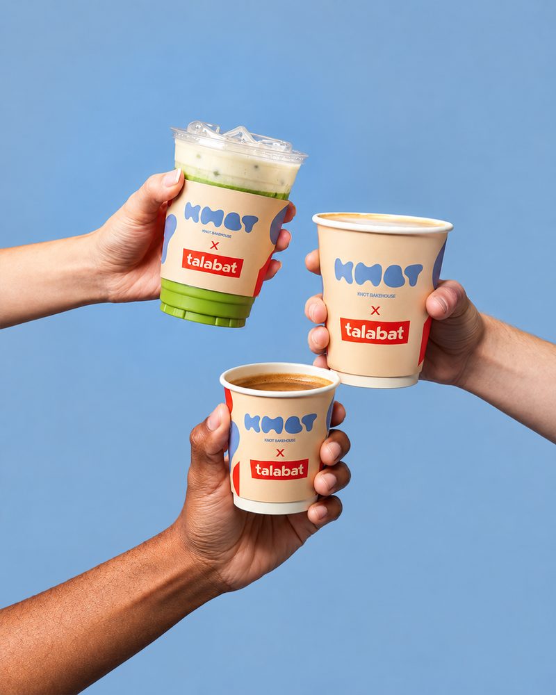 Three hands holding Knot Bakehouse and talabat cups together against a blue background