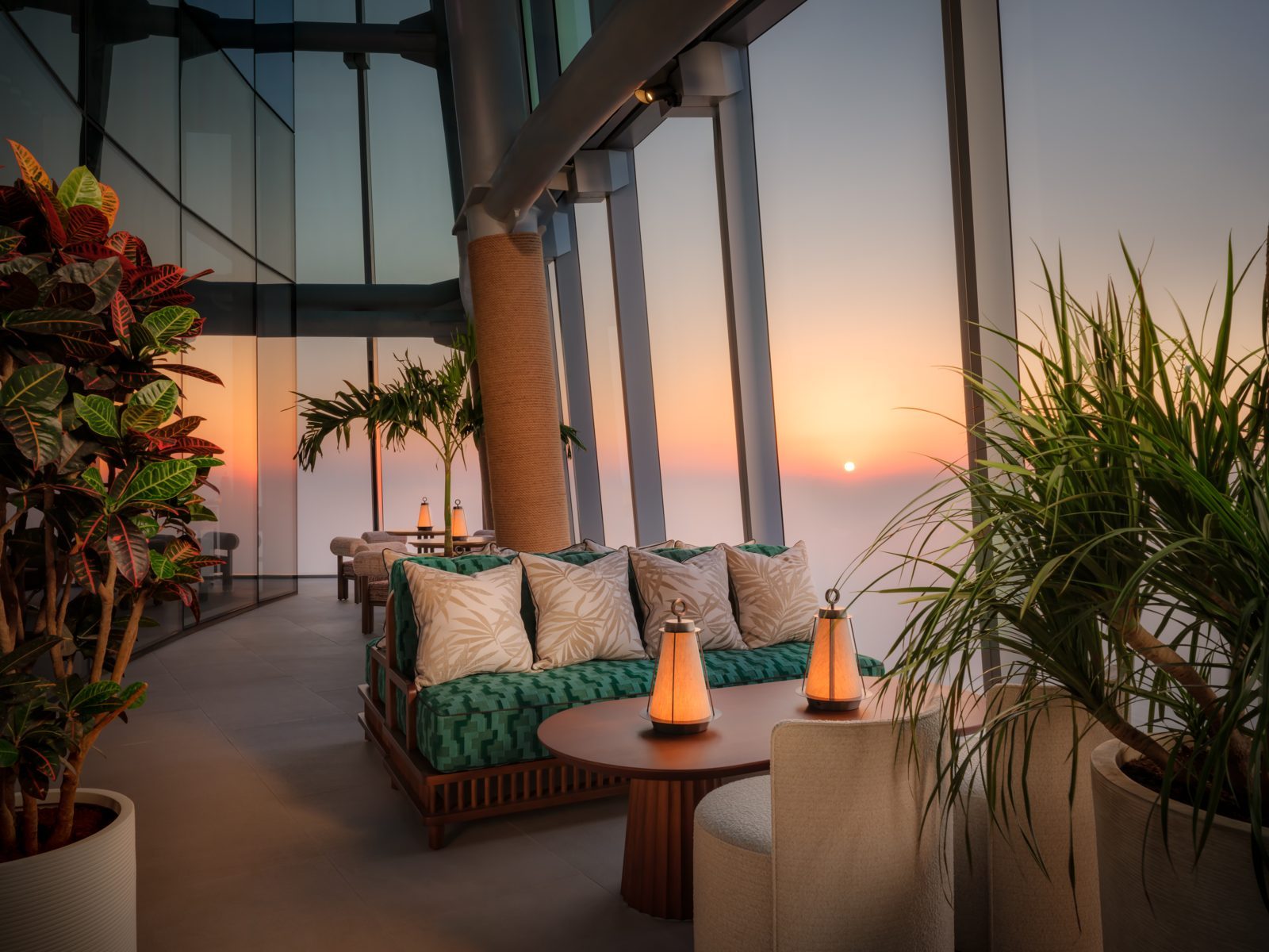 TATTU Sky Lounge terrace on Level 81 with green sofas, lanterns and plants against a sunset sky